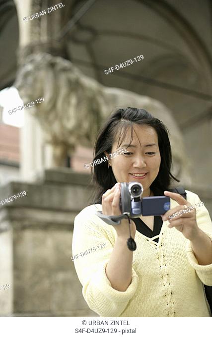 Young Asian woman with a camera standing in front of the ancient sculpture of a lion, selective focus
