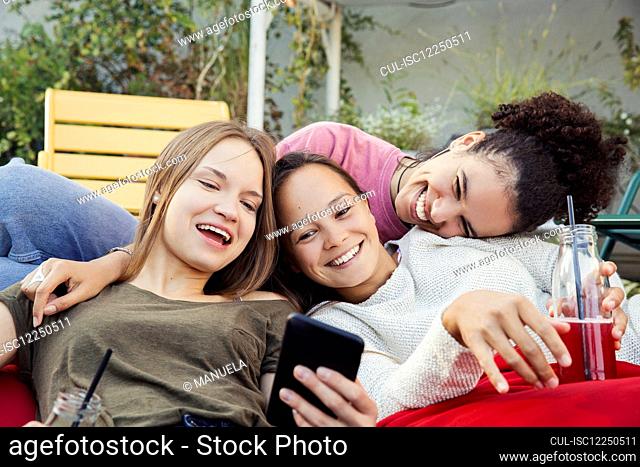 Three women lounging together, laughing and looking at a mobile phone