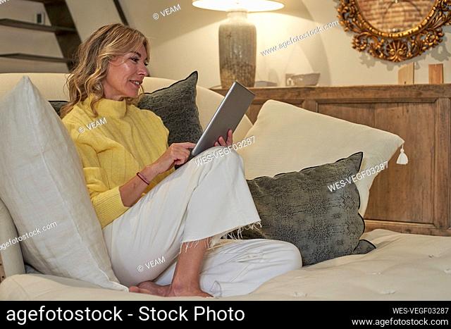Smiling mature woman in yellow sweater using digital tablet at home