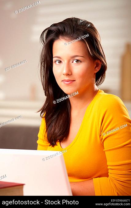 Teenage girl looking at camera smiling sitting at table with hands folded under chin