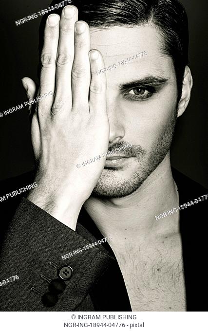 Portrait of young man covering his right eye with her hand on a black background. Studio shot