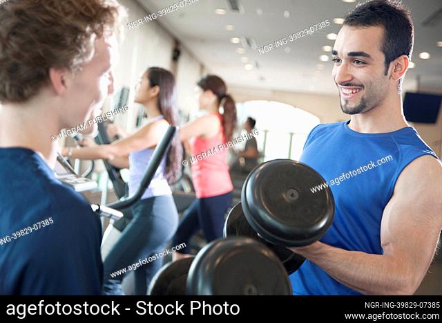 Two young men smiling and lifting weights in the gym