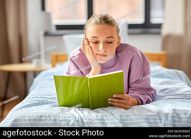 girl lying on bed and reading book at home