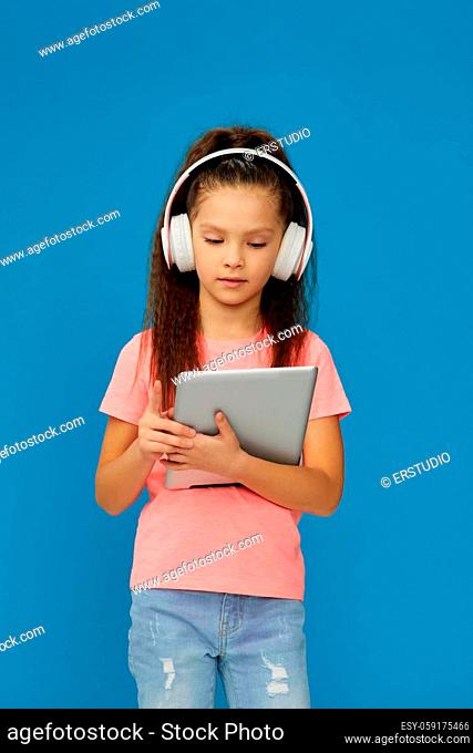 pretty little child girl in headphones using digital tablet on blue background