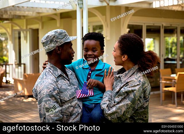 Front view of a young adult African American male and a young mixed race female soldier in the garden outside their home, holding and embracing their young son