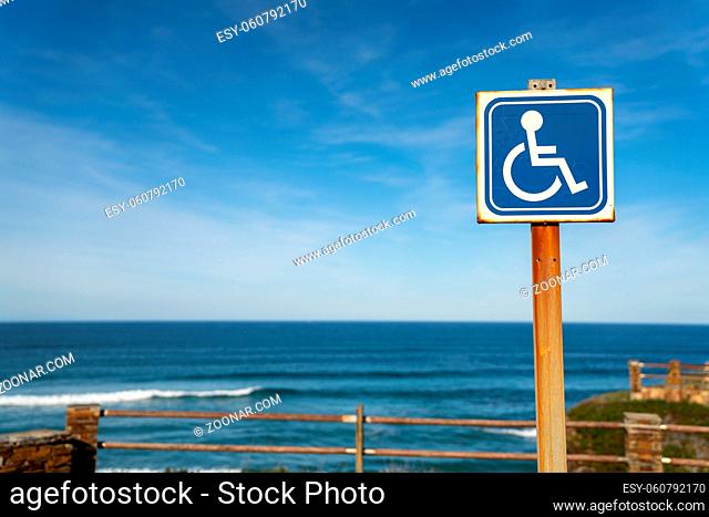 A sign for handicapped parking at a beach access with ocean behind