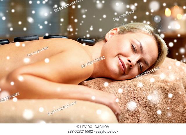 people, beauty, spa, winter and relaxation concept - close up of beautiful young woman having hot stone back massage in spa salon with snow effect
