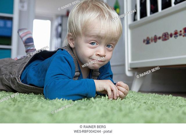 Portrait of funny little blond boy lying on green carpet at home