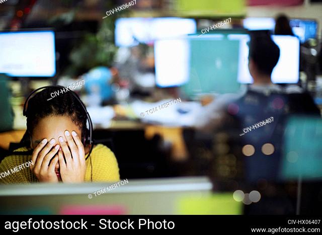 Tired, stressed businesswoman with head in hands at computer in office