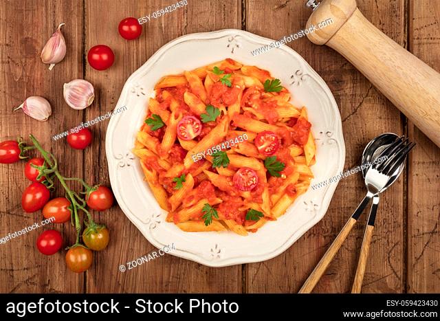 An overhead photo of a vibrant plate of pasta with tomato sauce. Penne rigate with ingredients, cherry tomatoes and garlic cloves