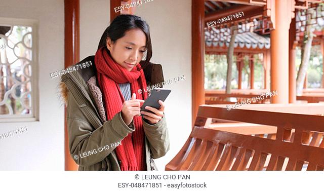 Woman surf the internet and sitting inside Chinese pavilion, woman wearing winter jacket