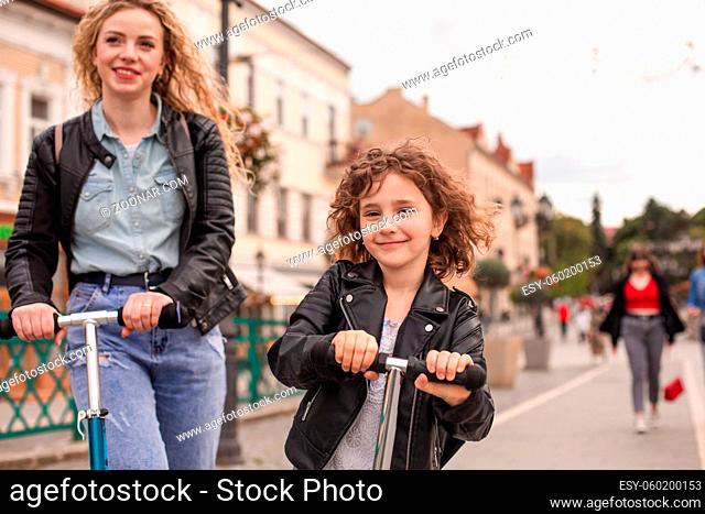 The happy little girl rides a scooter in the city. The girl with curly hair looks at the camera