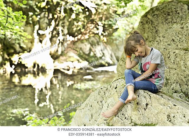 Girl sitting on a rock next to the Waterfall of the bucket in the Selva de Irati in Navarra, Spain