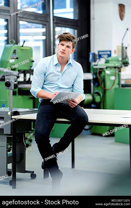Male engineer with document looking away while siting on desk in industry