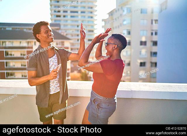 Happy young couple high fiving on sunny urban rooftop balcony