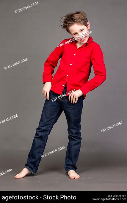 Handsome boy in a red shirt and jeans on a gray background. A child in the modeling business is posing