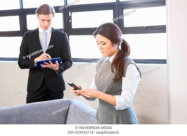 Businesswoman text messaging on smartphone and businessman using digital tablet