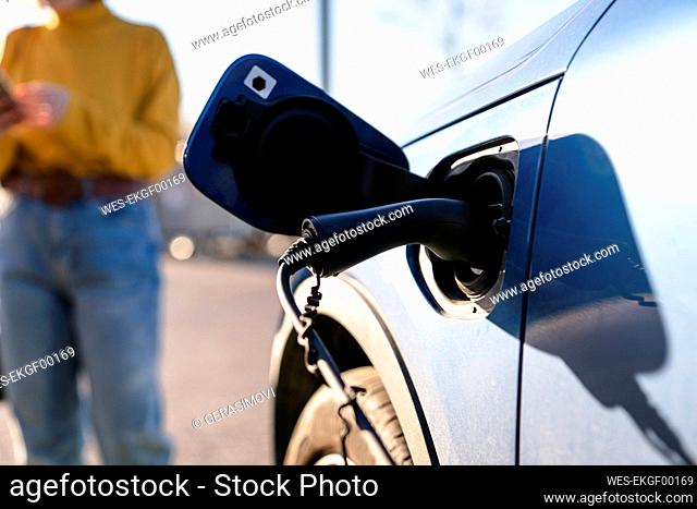 Electric car charging at station with woman standing in background