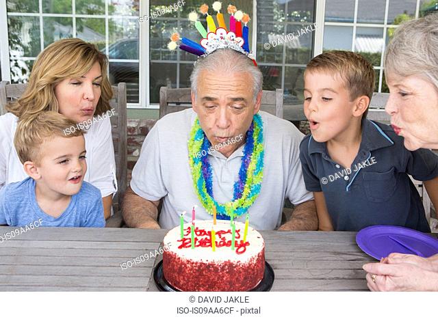Senior man blowing out candles on birthday cake with family