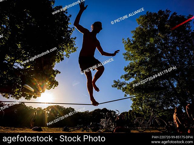 19 July 2022, Bavaria, Munich: A young man balances on a stretched slackline in the English Garden in the evening. Photo: Peter Kneffel/dpa