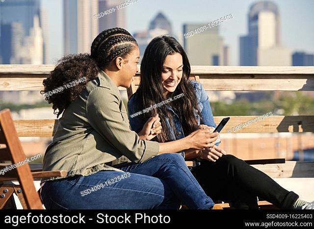Group of young co-workers hanging out on rooftop patio, two women looking at mobile phone