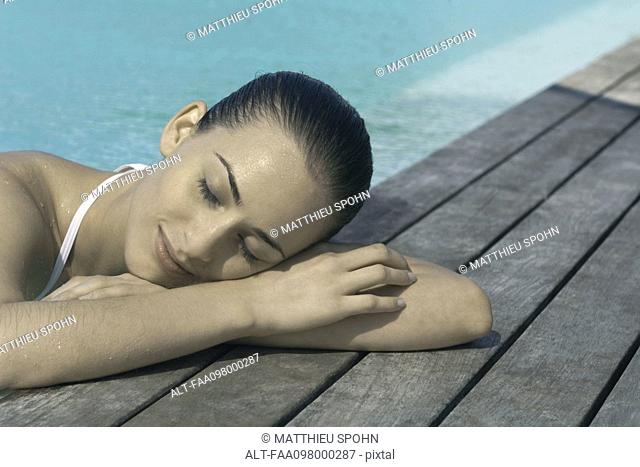 Young woman leaning on poolside, eyes closed