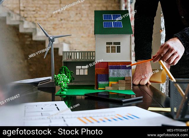 Hands of architect holding compass with house model on desk at construction site