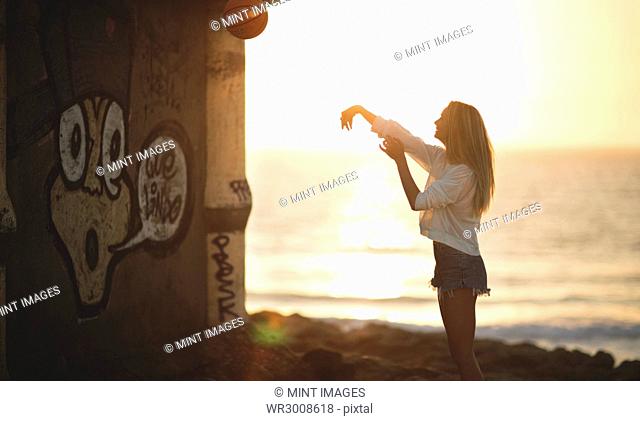 Young woman standing in front of a sunset throwing a basketball