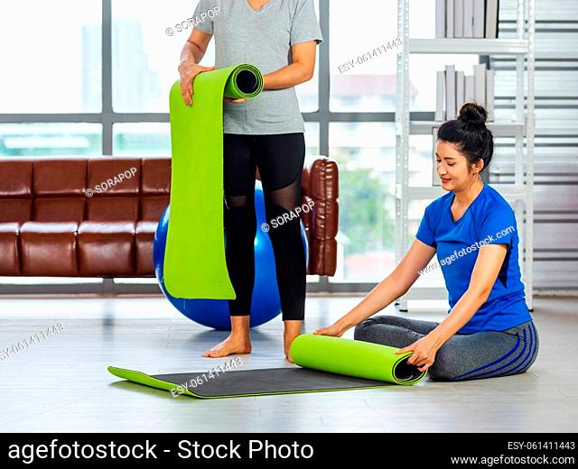 Asian adult and young woman smiling holding a yoga mat after yoga and exercise. Portrait of happy beautiful female standing hold yoga mat indoor studio
