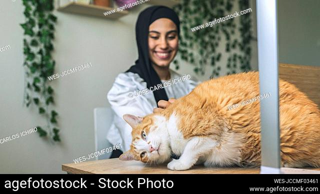 Smiling female professional stroking cat at desk in home office