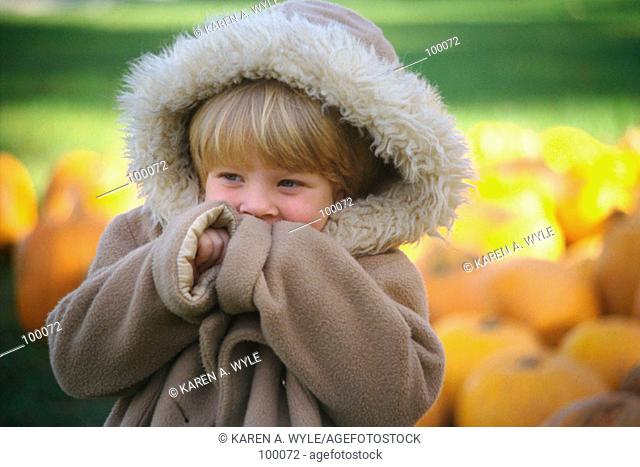 Young girl in oversized warm parka near pile of pumpkins