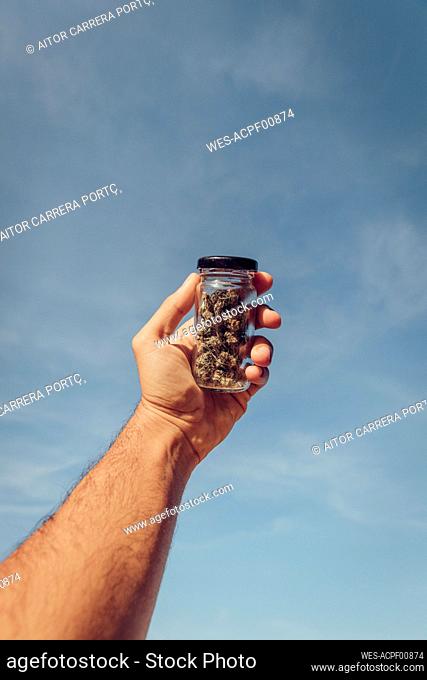 Man holding small marijuana jar against sky