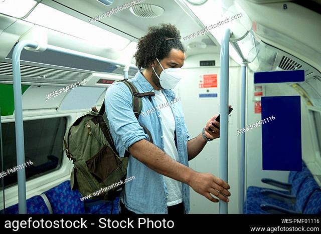Man wearing protective mask standing in underground train looking at cell phone, London, UK