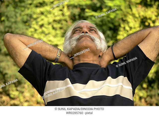 Elderly gentleman in dark blue T-shirt over sixty years of age resting and thinking by looking in sky in park MR686A