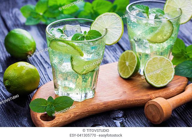 Two glasses of refreshing cold mojito with ice on a black wooden table
