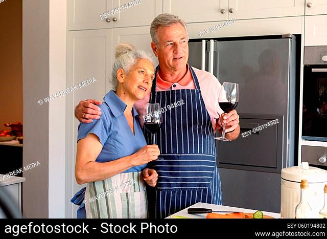 Relaxed caucasian senior couple standing in kitchen, drinking wine and preparing meal together