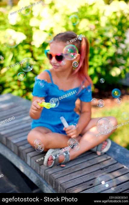little child girl blowing soap bubbles in summer park. focus on bubbles