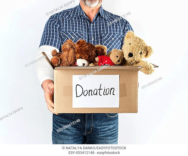 a man in a blue shirt and jeans holding a big brown paper box with children's toys, help concept for the poor, white background