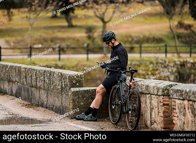 Cyclist using mobile phone leaning on wall