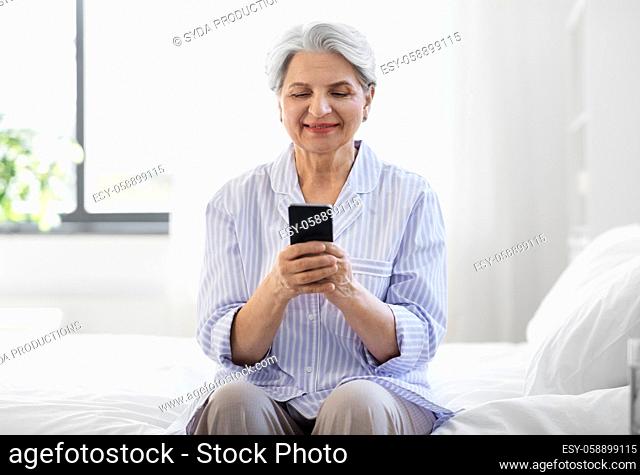 happy senior woman with smartphone on bed at home