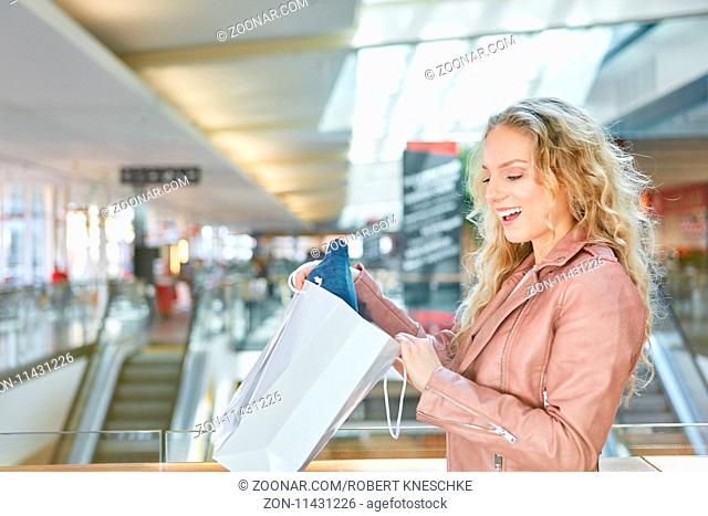 Junge blonde Frau blickt überrascht in eine Einkaufstüte nach dem Shopping