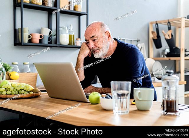 Tired man using laptop at kitchen counter