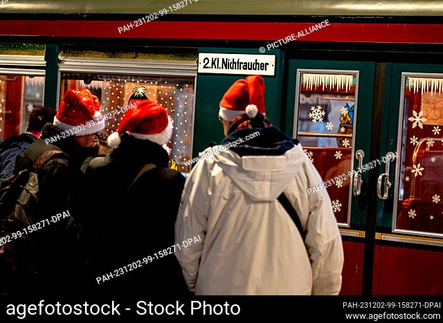 02 December 2023, Berlin: Three people wearing Christmas hats stand in front of the Christmas train of the Historische S-Bahn association at Grünau S-Bahn...