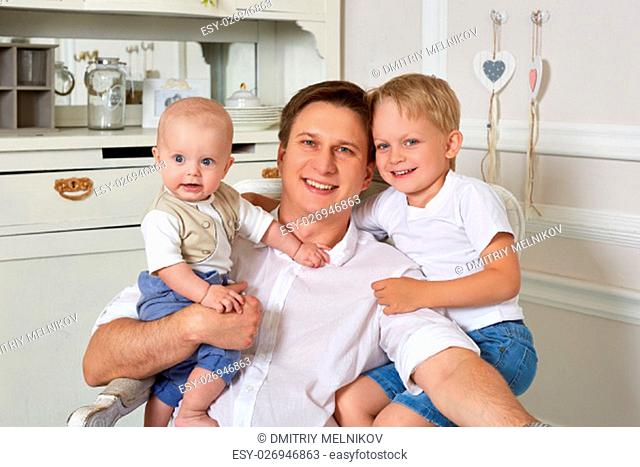 Happy father with two small sons are sitting in an armchair in the room