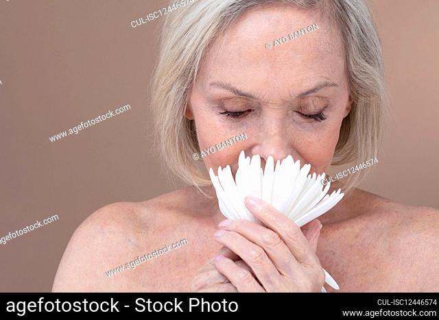 Studio shot of shirtless senior woman smelling white flower