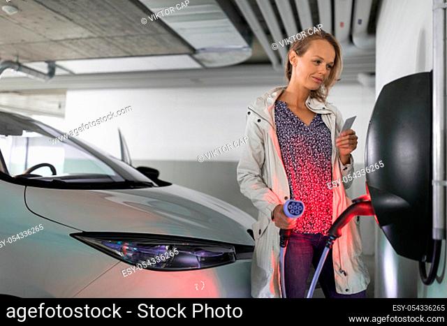 Young woman charging an electric vehicle in an underground garage equiped with e-car charger. Car sharing concept