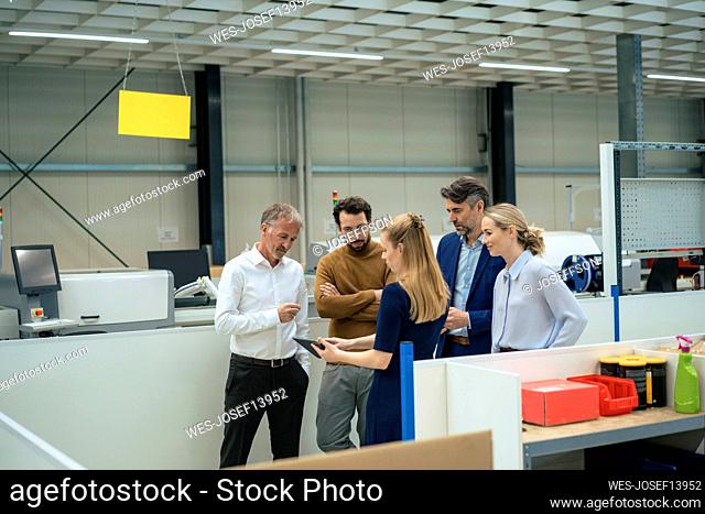 Businesswoman discussing with colleagues over tablet PC in industry