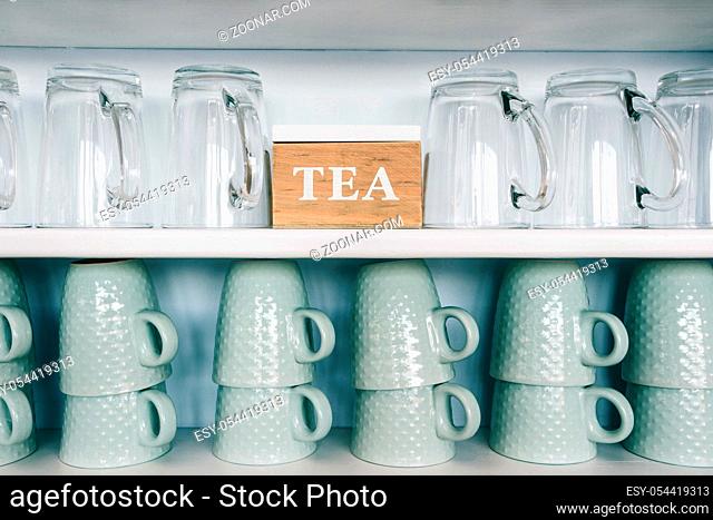 tea cups and coffee mugs on a kitchen shelf with a tea box Rack focus. Close up. wooden shelf