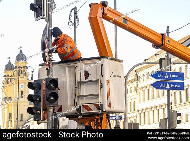 19 December 2023, Bavaria, Munich: A man in a lifting platform is laying cable harnesses for the traffic light control system across Ludwigstrasse near...
