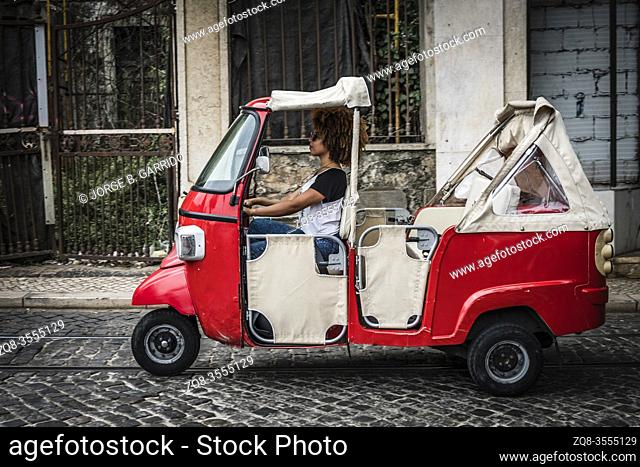 Tourists enjoy a ride in a tuk tuk, three wheeled vehicle in the center of Lisbon, Portugal